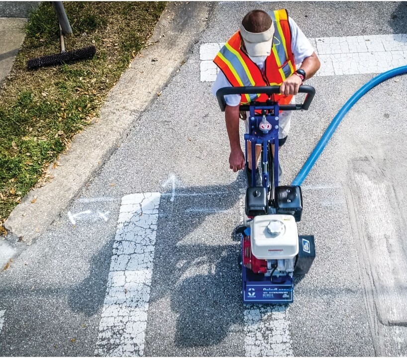 man using striping equipment on roadway to refinish crosswalk