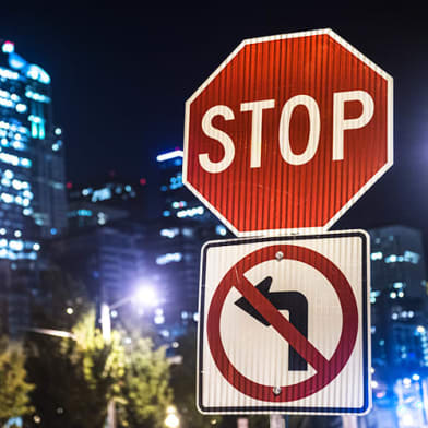 stop sign and no left turn sign at night with the city in the backround.
