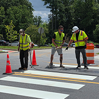 3 men surveying and painting a crosswalk in the road
